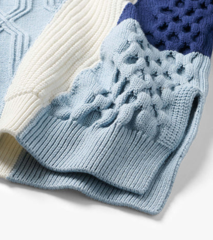 Close-up of mixed pattern sweater showing light blue, cream, and navy panels with ribbed, cable, and bobble knit details