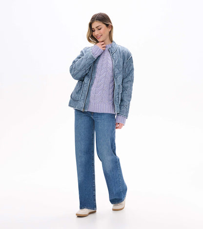 Speckle lilac cable-knit sweater styled under a faded blue quilted jacket with jeans