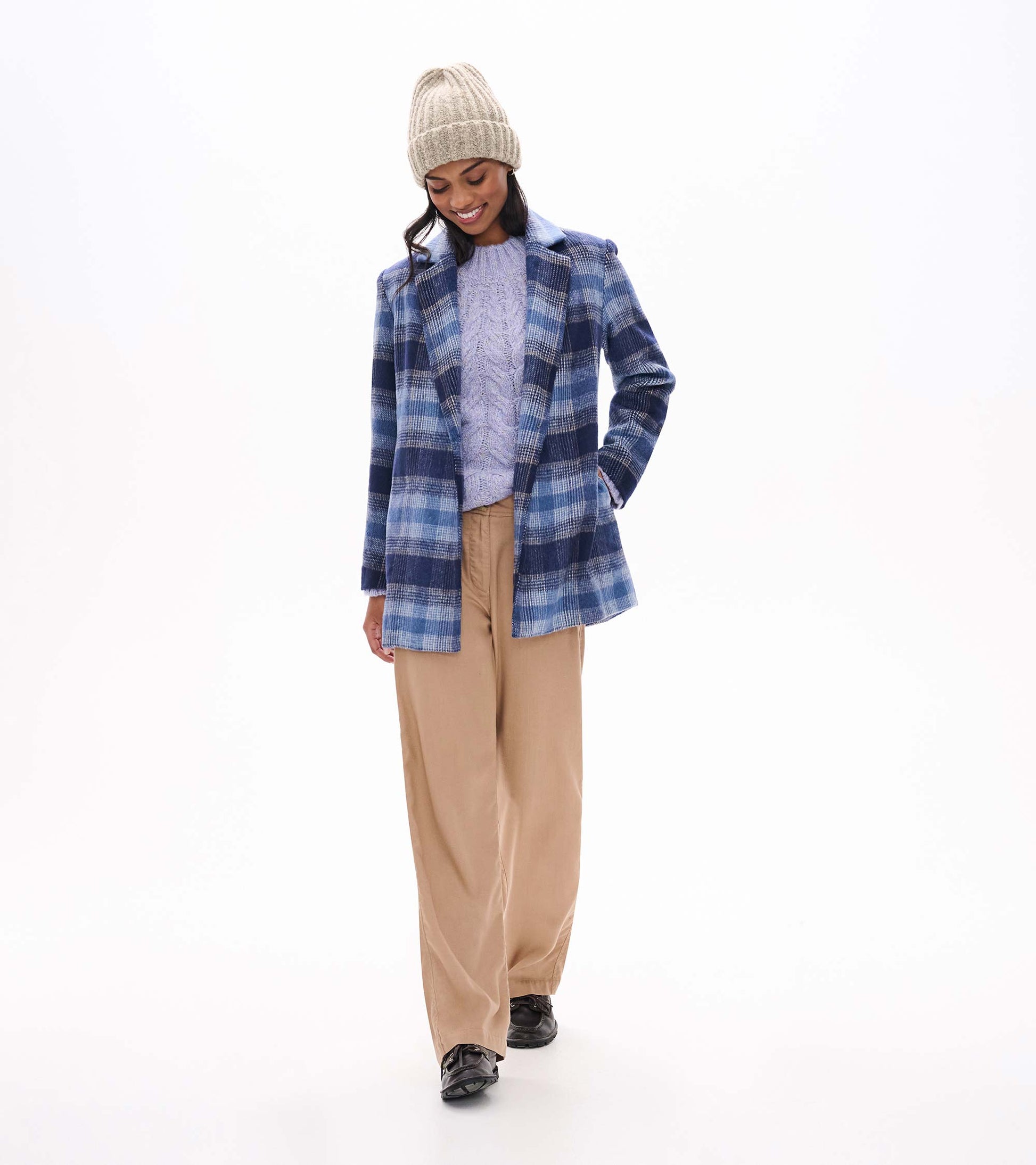 Speckle lilac cable-knit sweater styled under a blue plaid coat with tan pants and a knit beanie