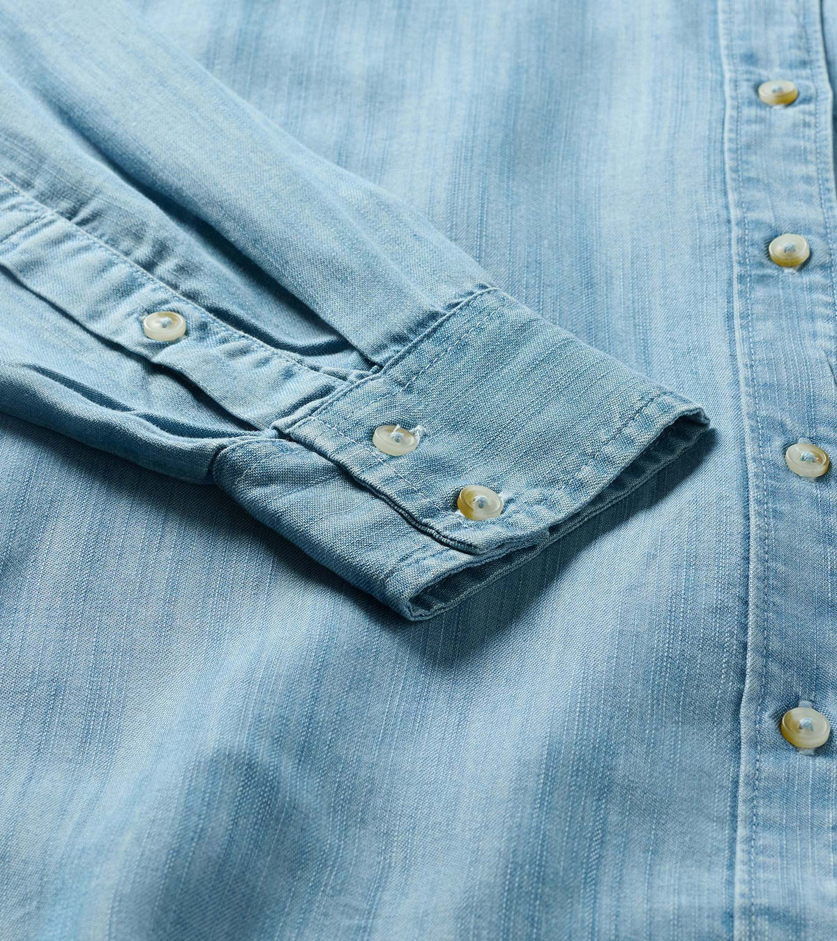 Close-up of light blue wash button-down shirt showing front buttons and button cuff detail
