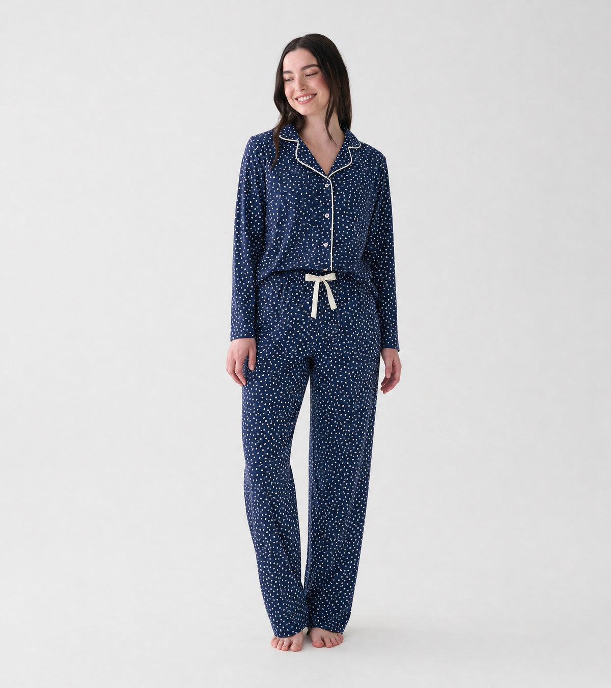 Woman wearing navy polka dot pajama set with white piping and drawstring pants, front view