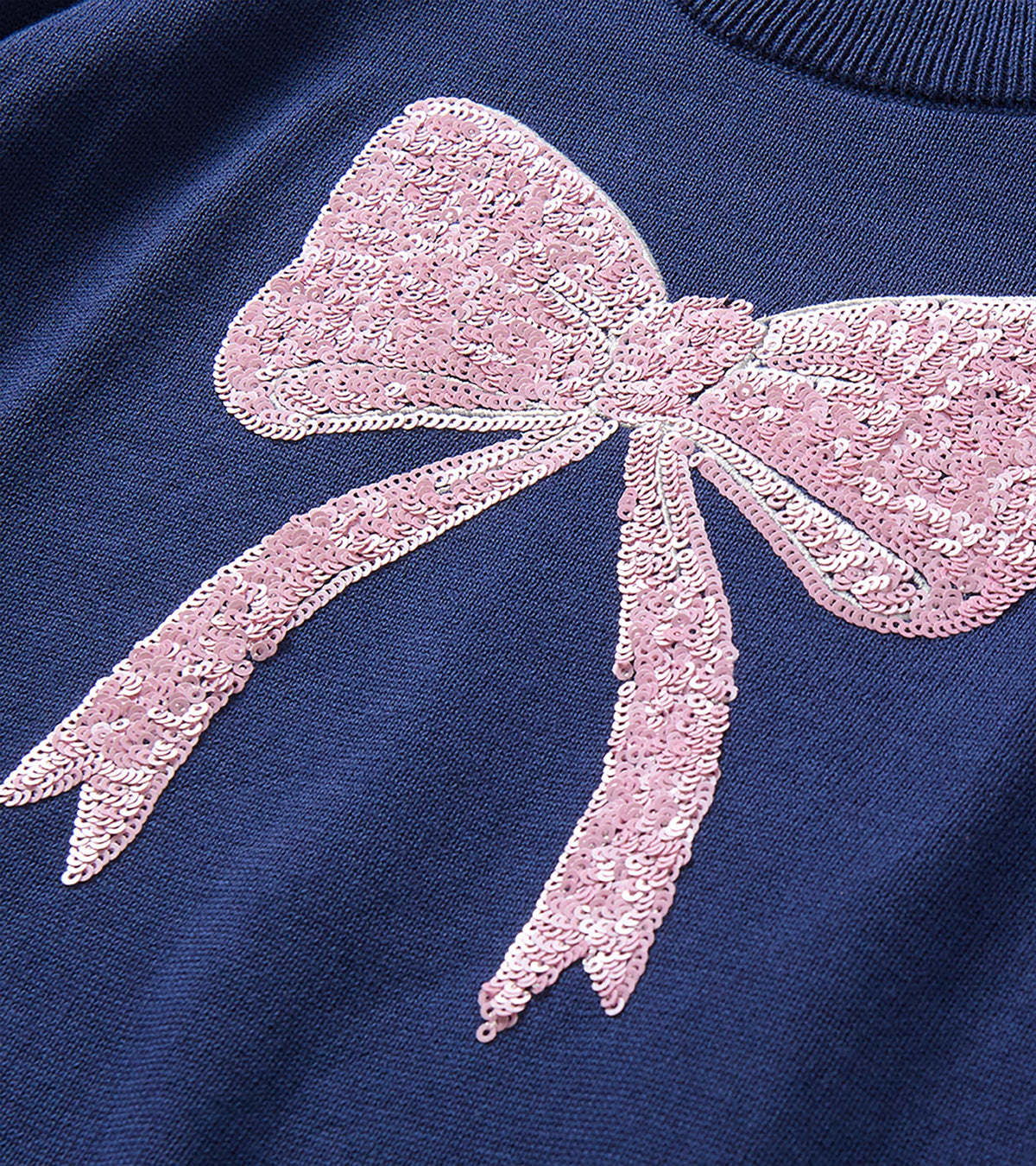 Close-up of pink sequin bow detail on the front of a navy sweater
