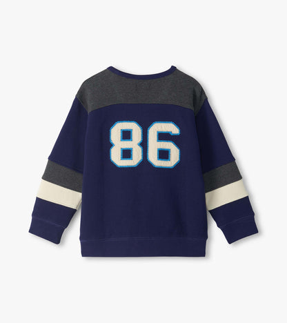 Back view of boys blue pullover top with gray yoke, cream sleeve stripes, and large 86 applique