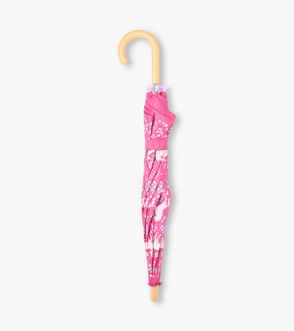Closed pink unicorn print umbrella with curved wooden-look handle and matching strap