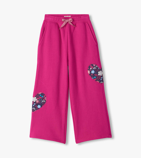 Bright pink wide leg track pants with side pockets, drawstring waist, and floral heart patches on the legs