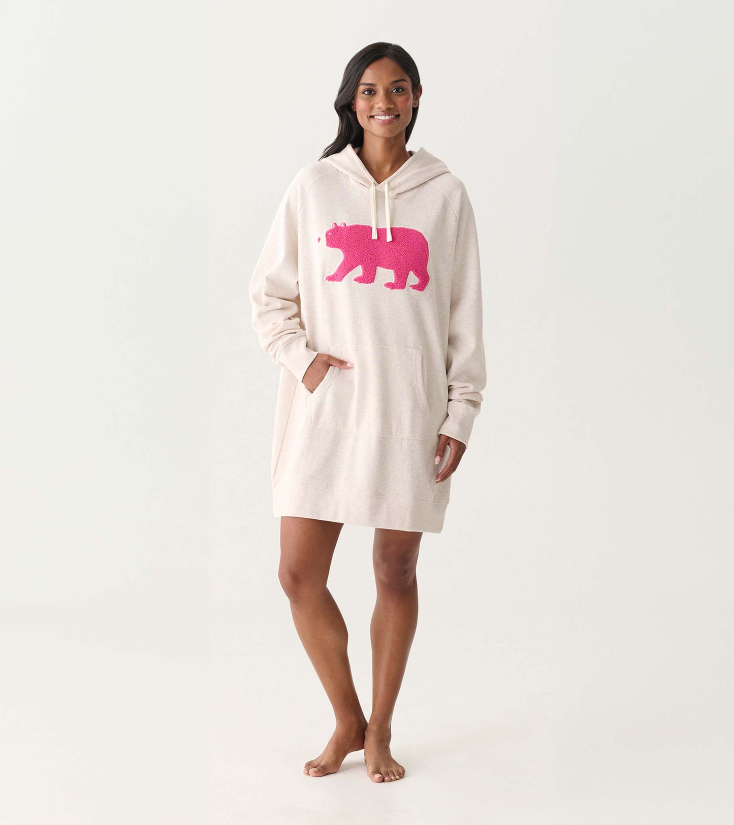 Cream oversized hoodie dress with pink bear graphic, hood, drawstrings, and front pocket, worn by model