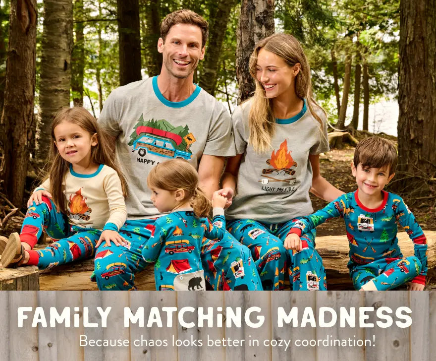 Promotes family matching sleepwear. Showing family of four wearing coordinated camping-themed pajamas in a forest.