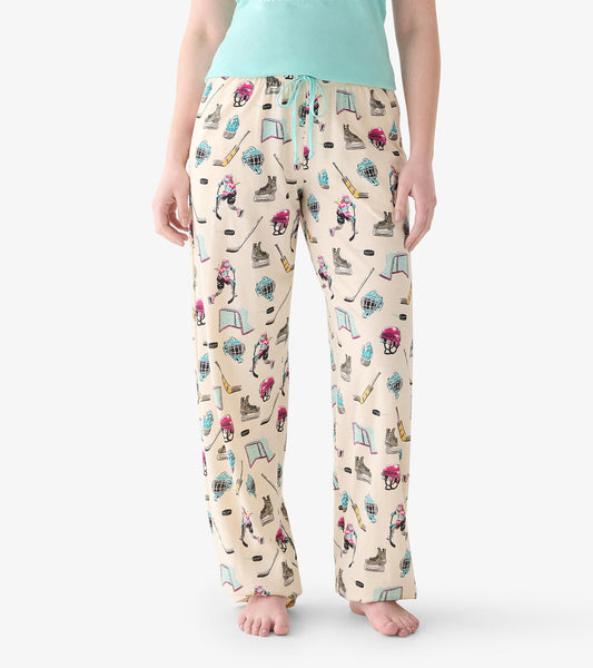 Close-up of cream pajama pants with teal drawstring and hockey print of skates, sticks, pucks, helmets and nets