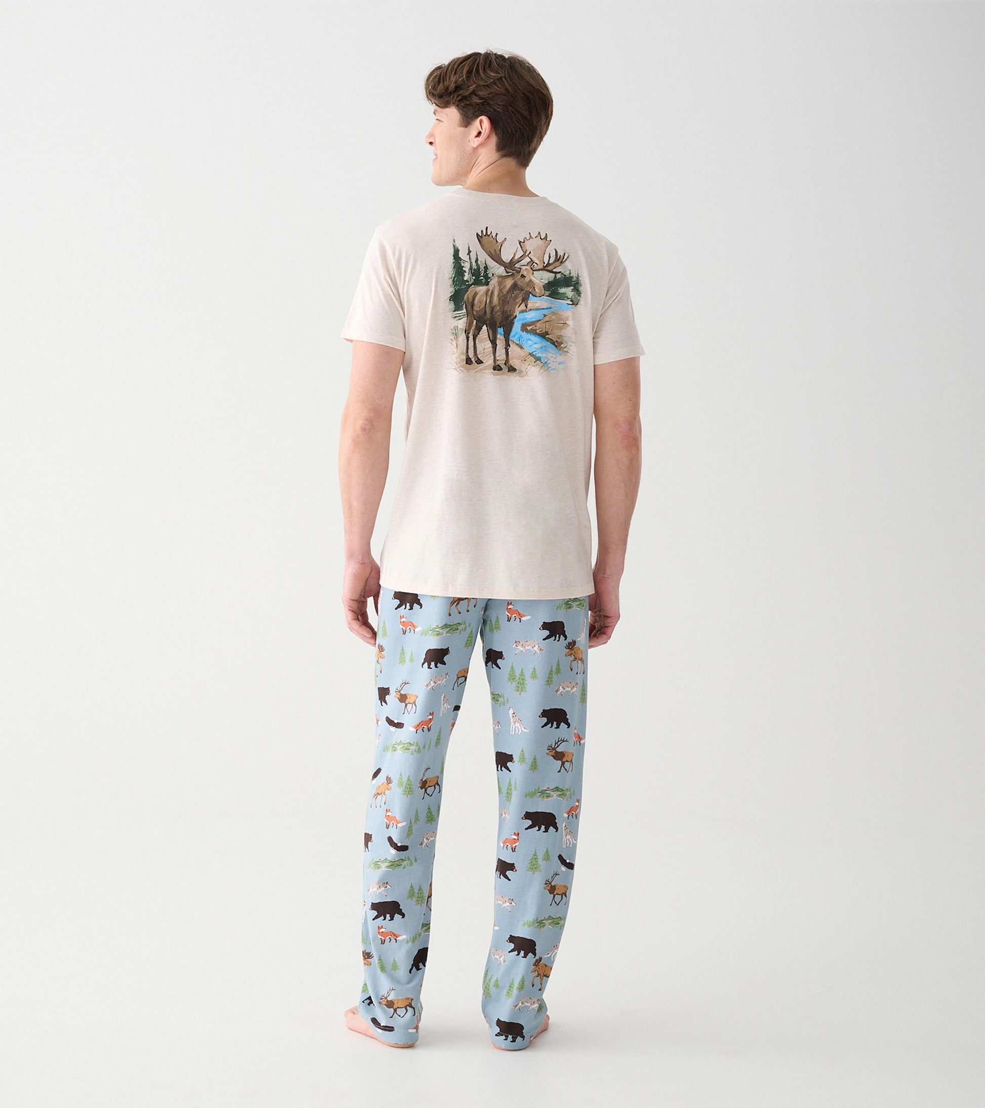 Model wearing light blue wilderness print pajama pants and beige tee with moose graphic, back view