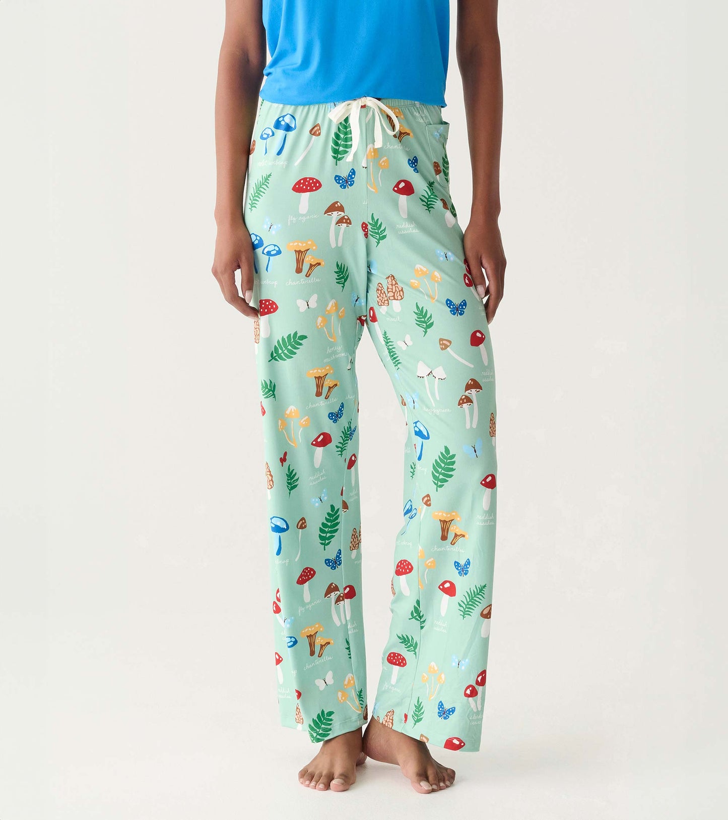 Mint green pajama pants with colorful mushroom, leaf, and butterfly print, shown on model