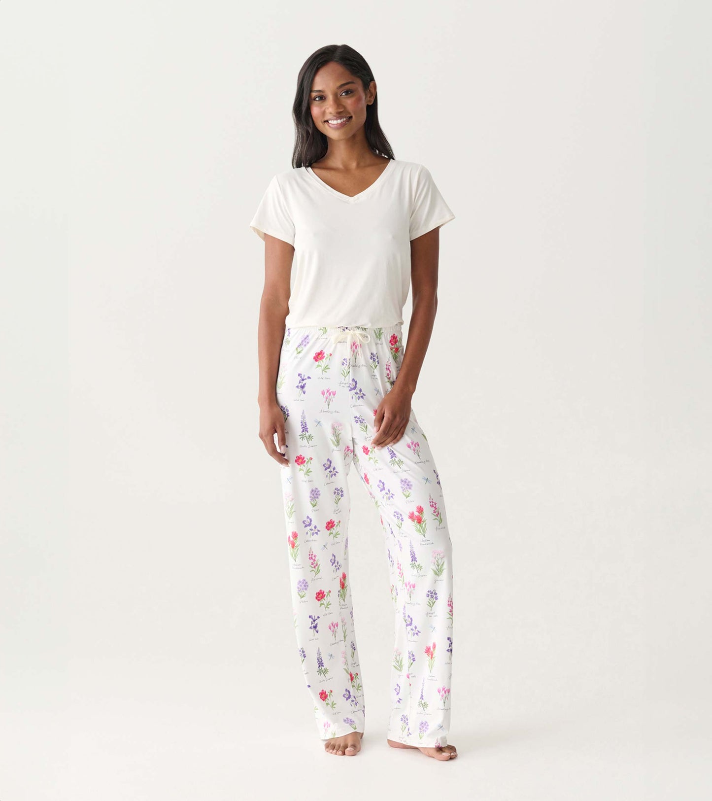 White pajama pants with colorful wildflower print, shown on a model with a white V-neck top.