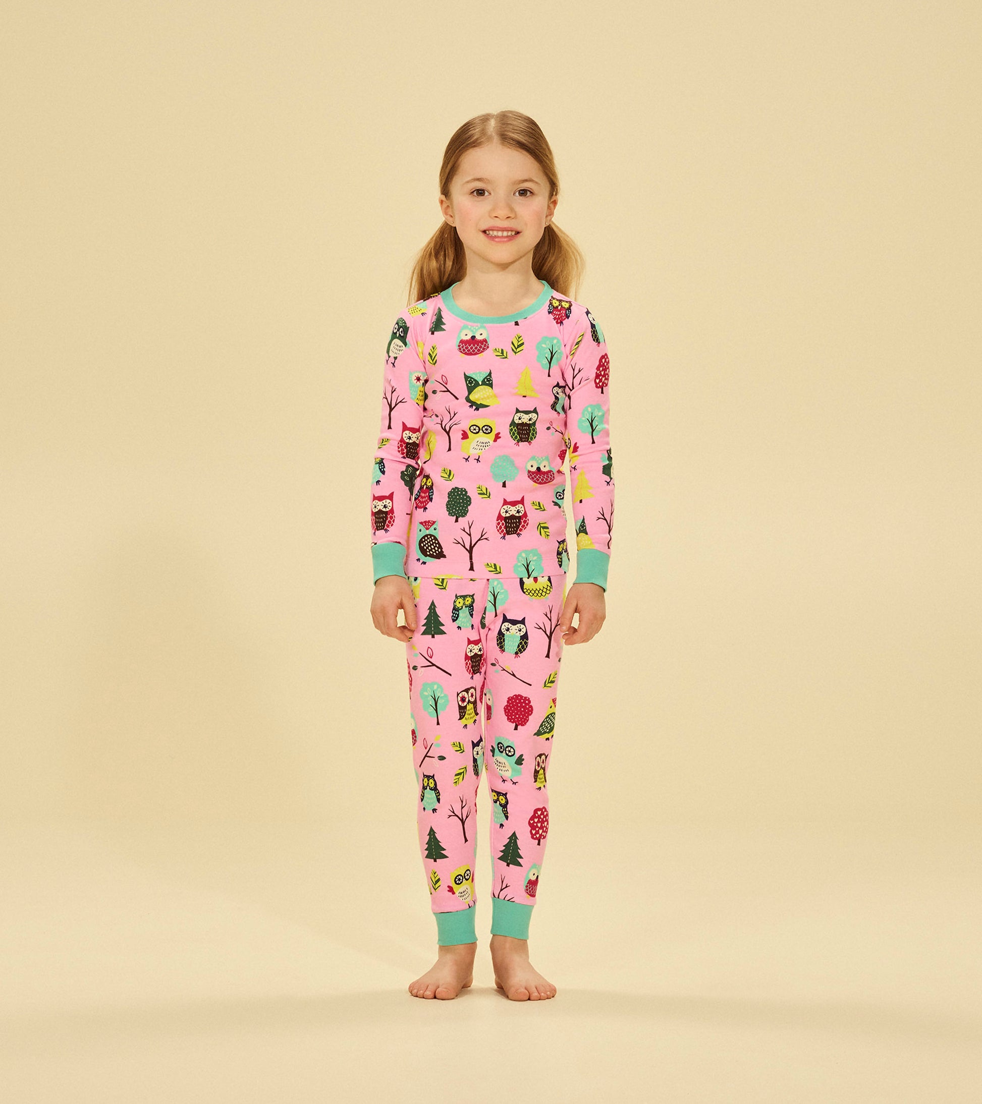 Pink pajama set featuring colorful owl and tree patterns, with long sleeves and matching pants, suitable for kids.
