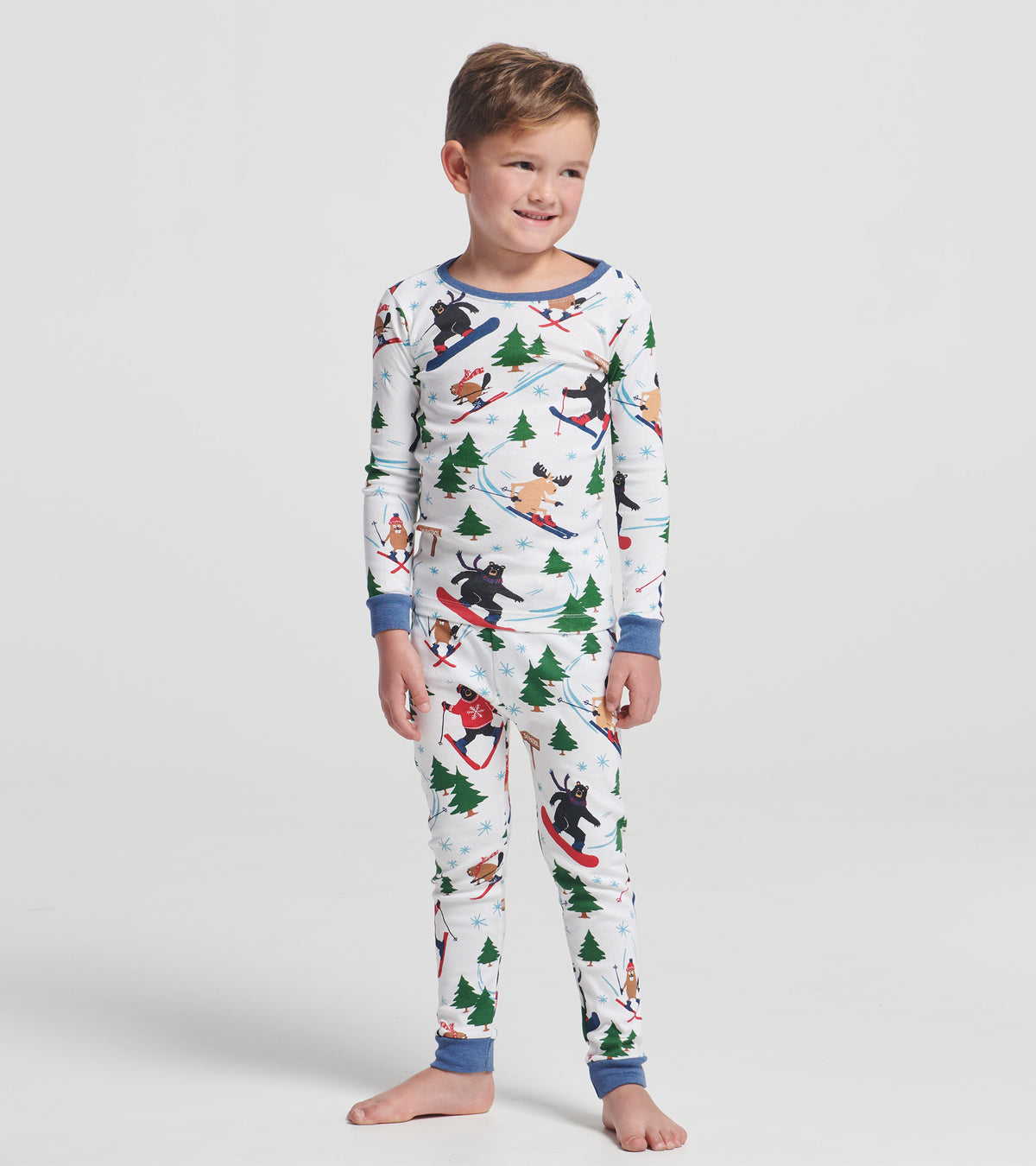 Child wearing white ski print pajama set with blue trim, featuring bears, moose, trees and snowflakes