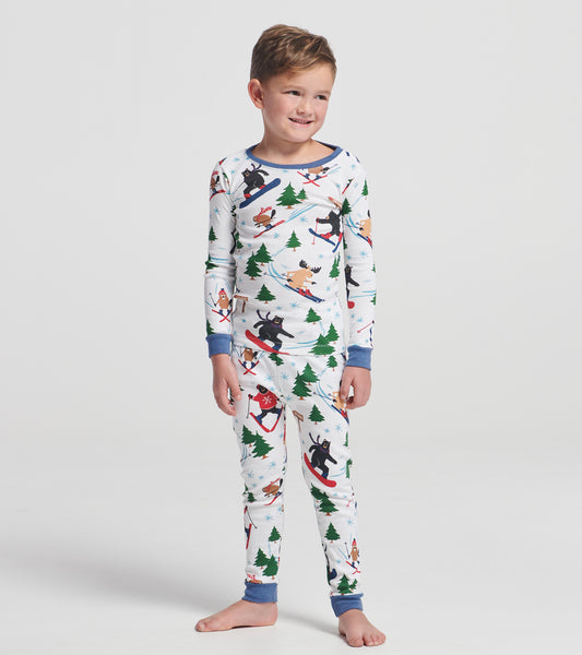 Child wearing white ski print pajama set with blue trim, featuring bears, moose, trees and snowflakes
