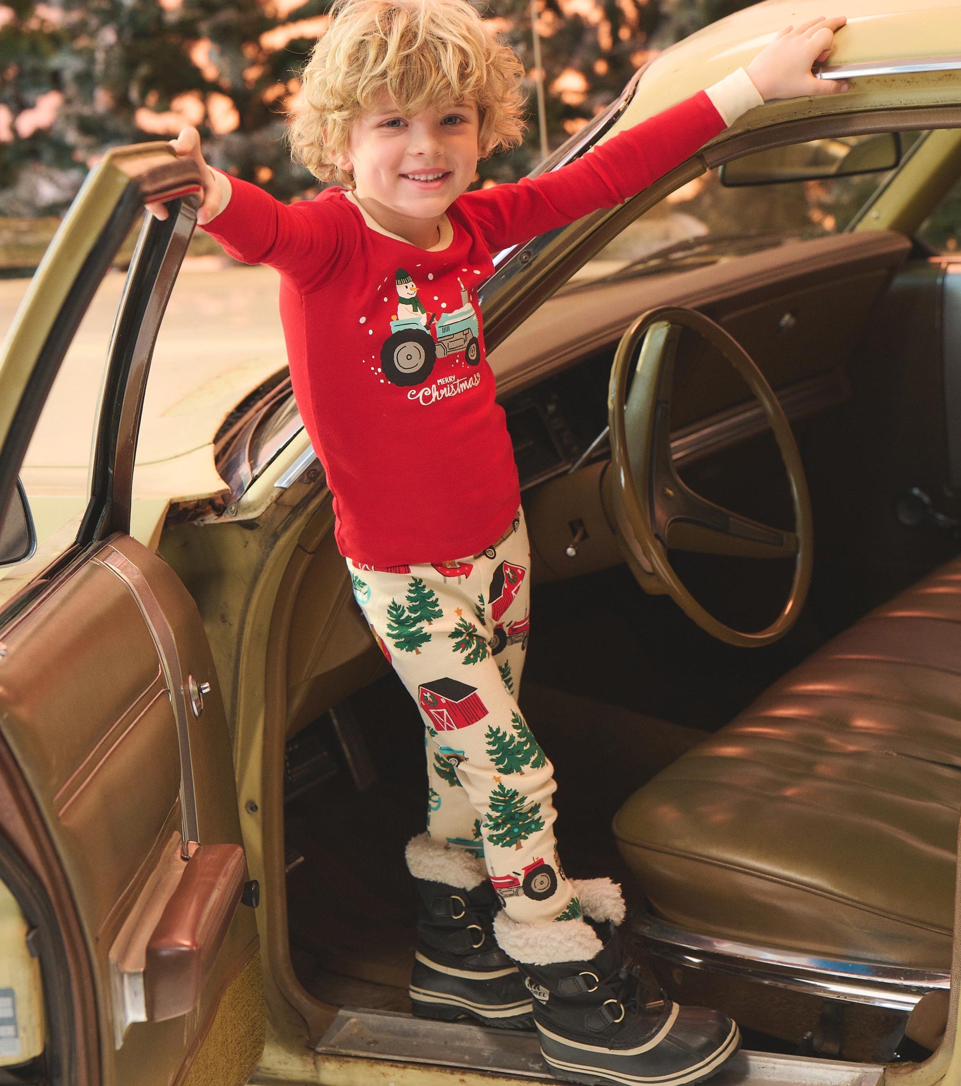 Red long-sleeve pajama top with tractor graphic, paired with cream pants featuring Christmas trees and barns.