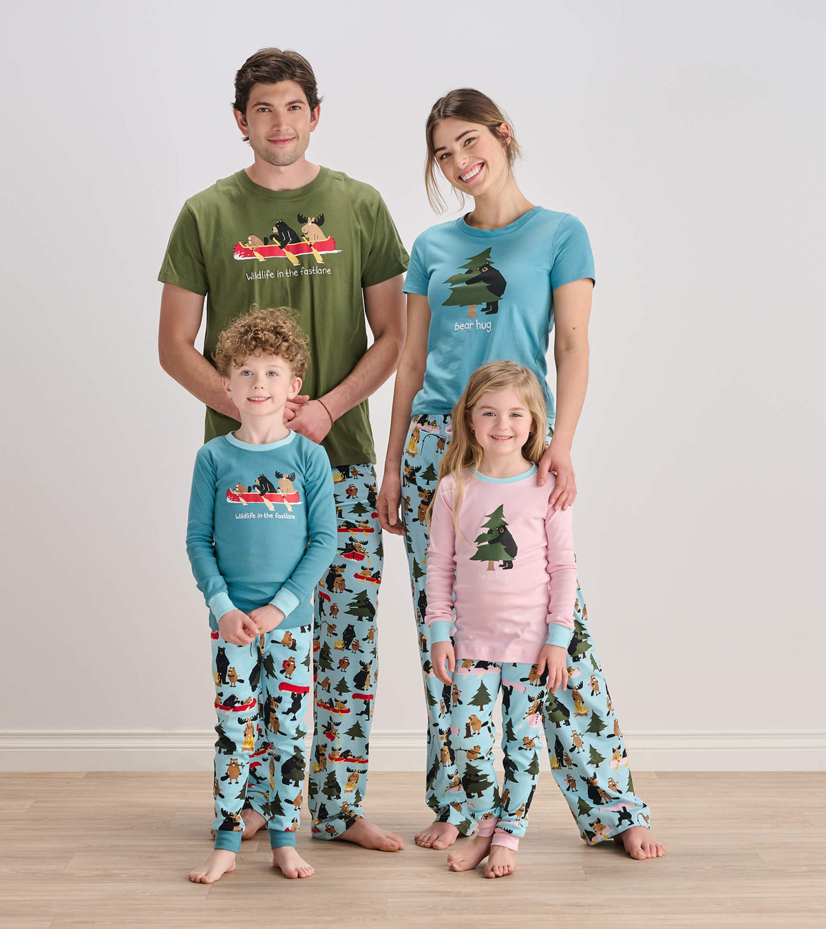 Family wearing matching wildlife print pajamas; kids in blue and pink sets with animal and tree graphics