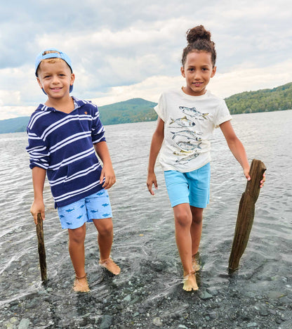 Two boys wearing light blue shorts standing in shallow water by a lake