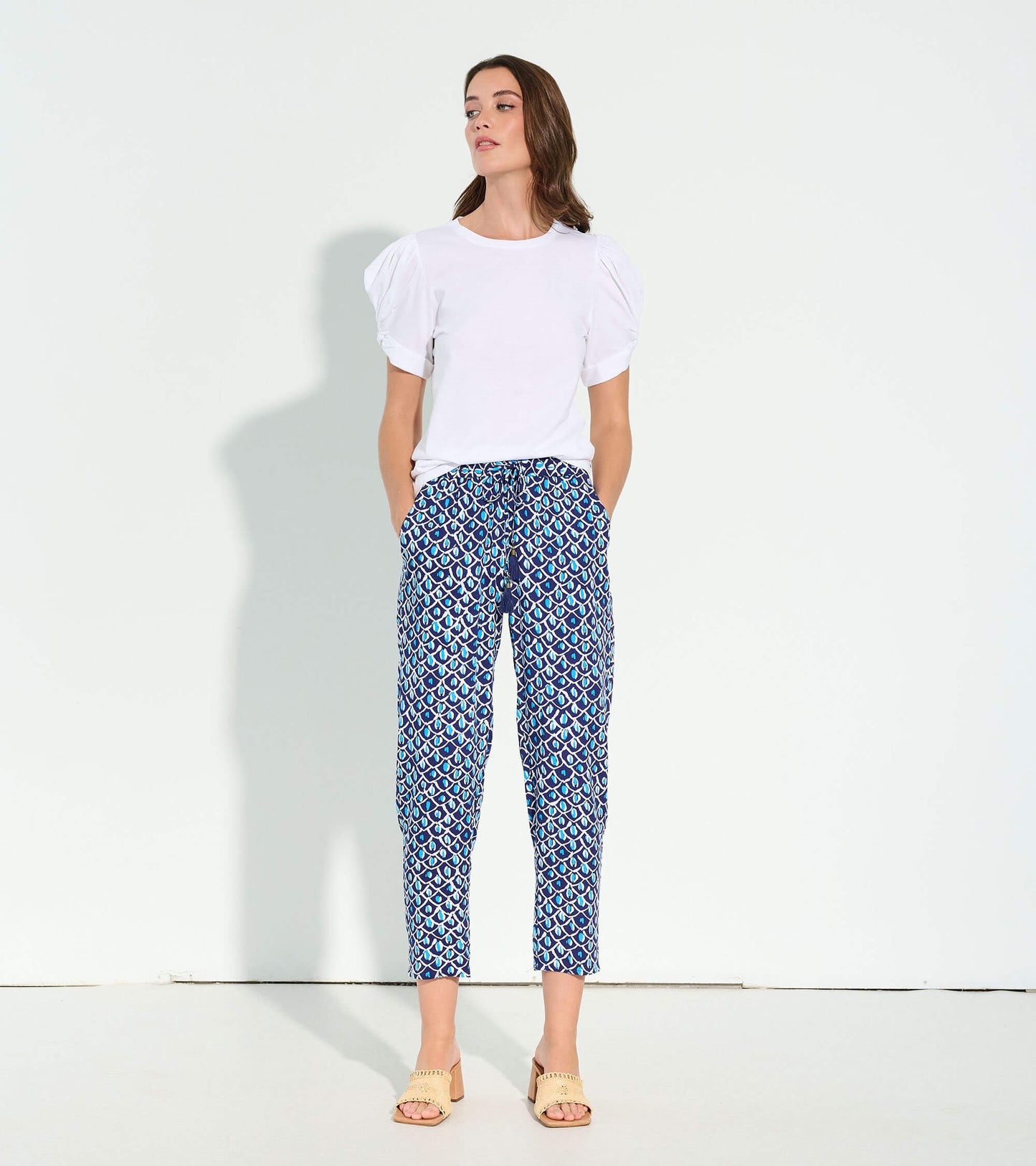 White short-sleeve tee with puffed sleeves, paired with patterned blue pants, worn by a model standing.
