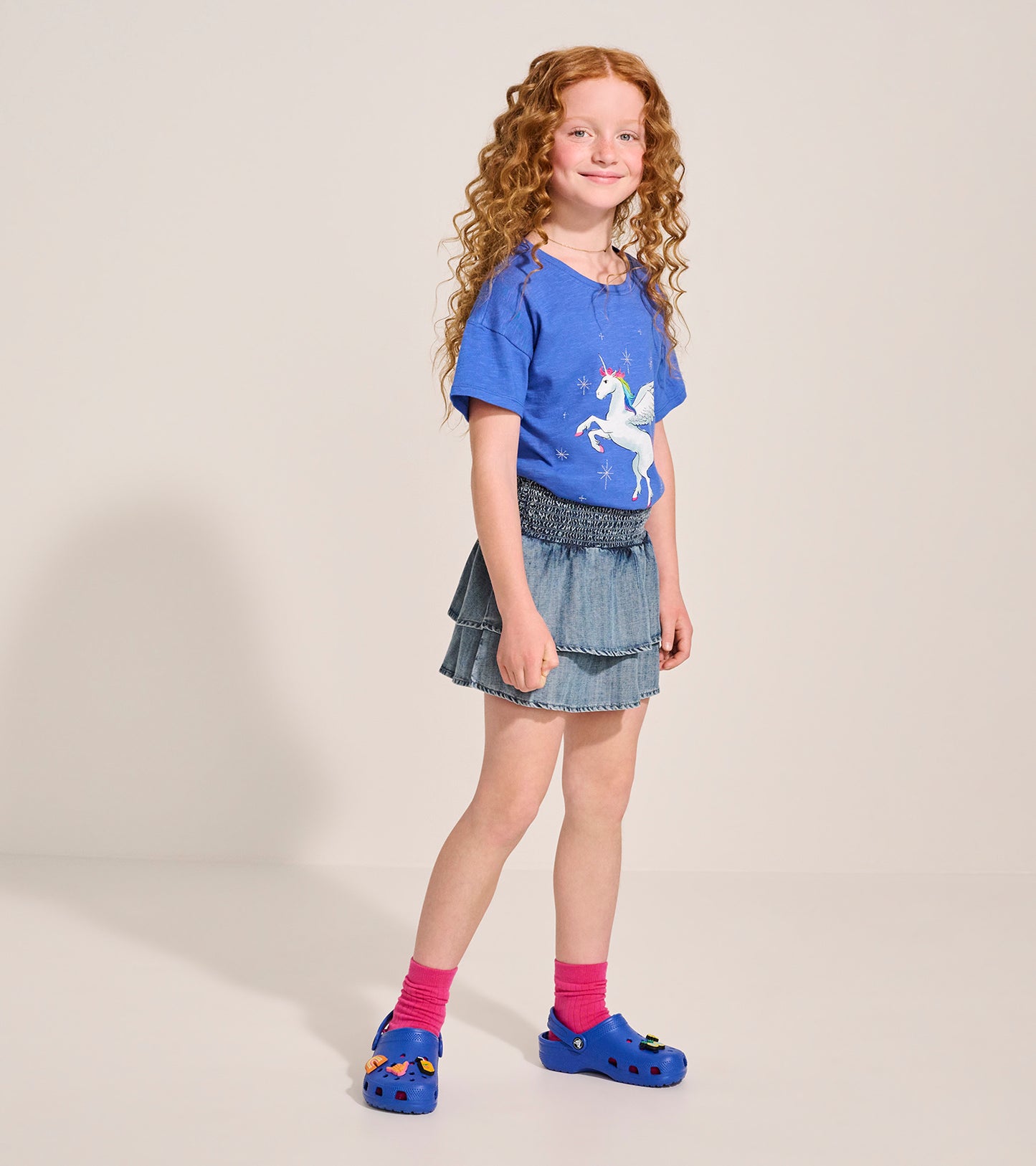 Light blue Tencel smocked skirt with tiered ruffles, paired with a unicorn graphic tee and colorful clogs.