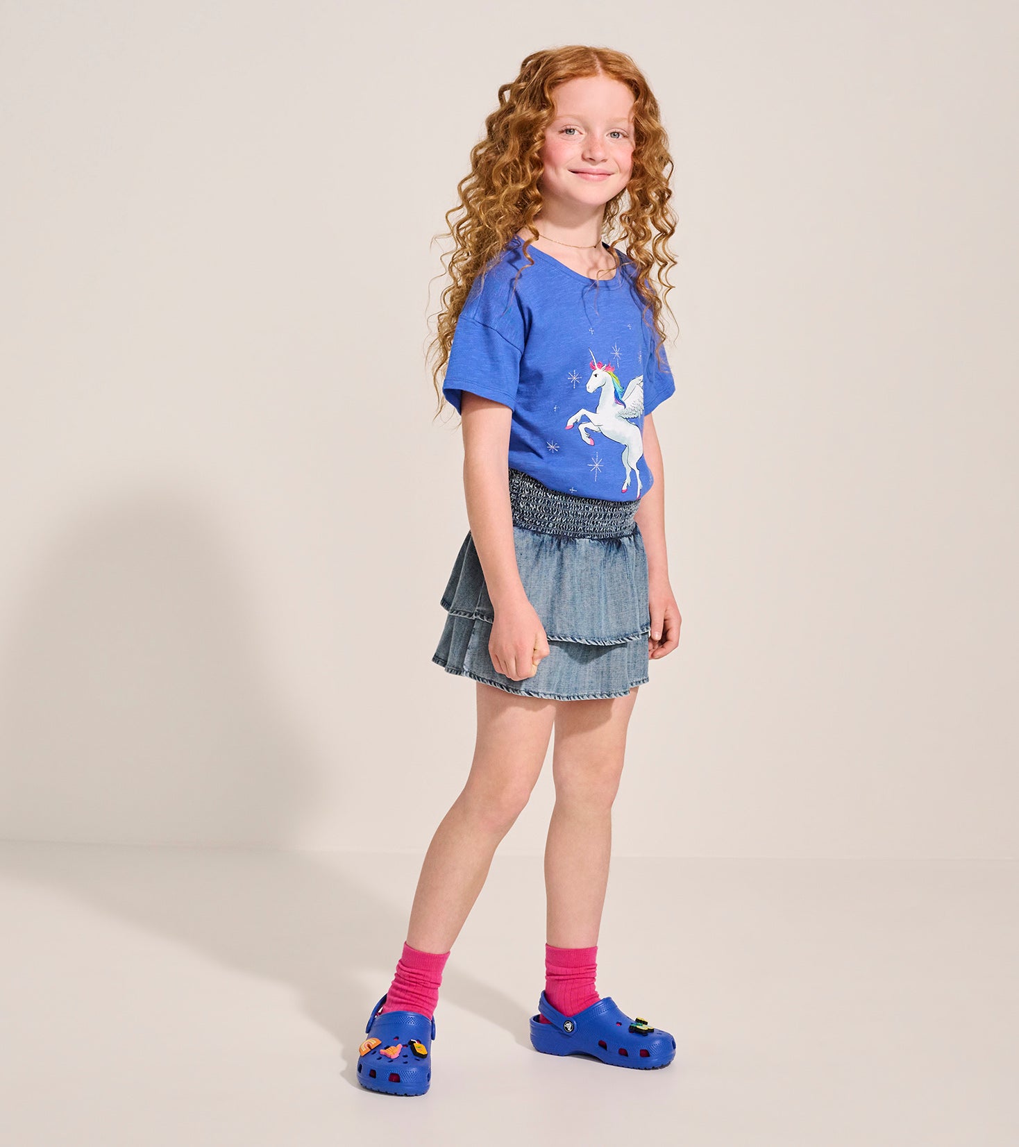 Light blue Tencel smocked skirt with tiered ruffles, paired with a unicorn graphic tee and colorful clogs.