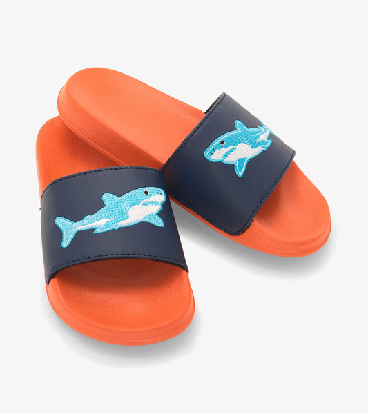 Navy slide sandals with orange soles featuring a blue shark design on the strap. Suitable for kids.