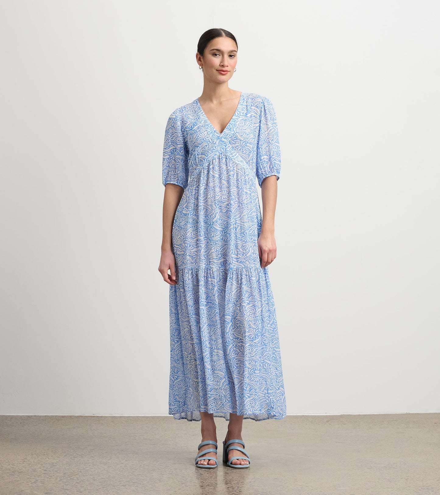 Light blue maxi dress with a floral pattern, v-neckline, and short puff sleeves, styled with strappy sandals.