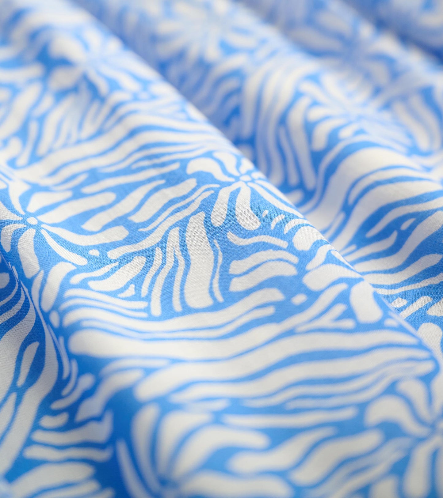 Blue fabric featuring a groovy white floral pattern, showcasing a soft, flowing texture.