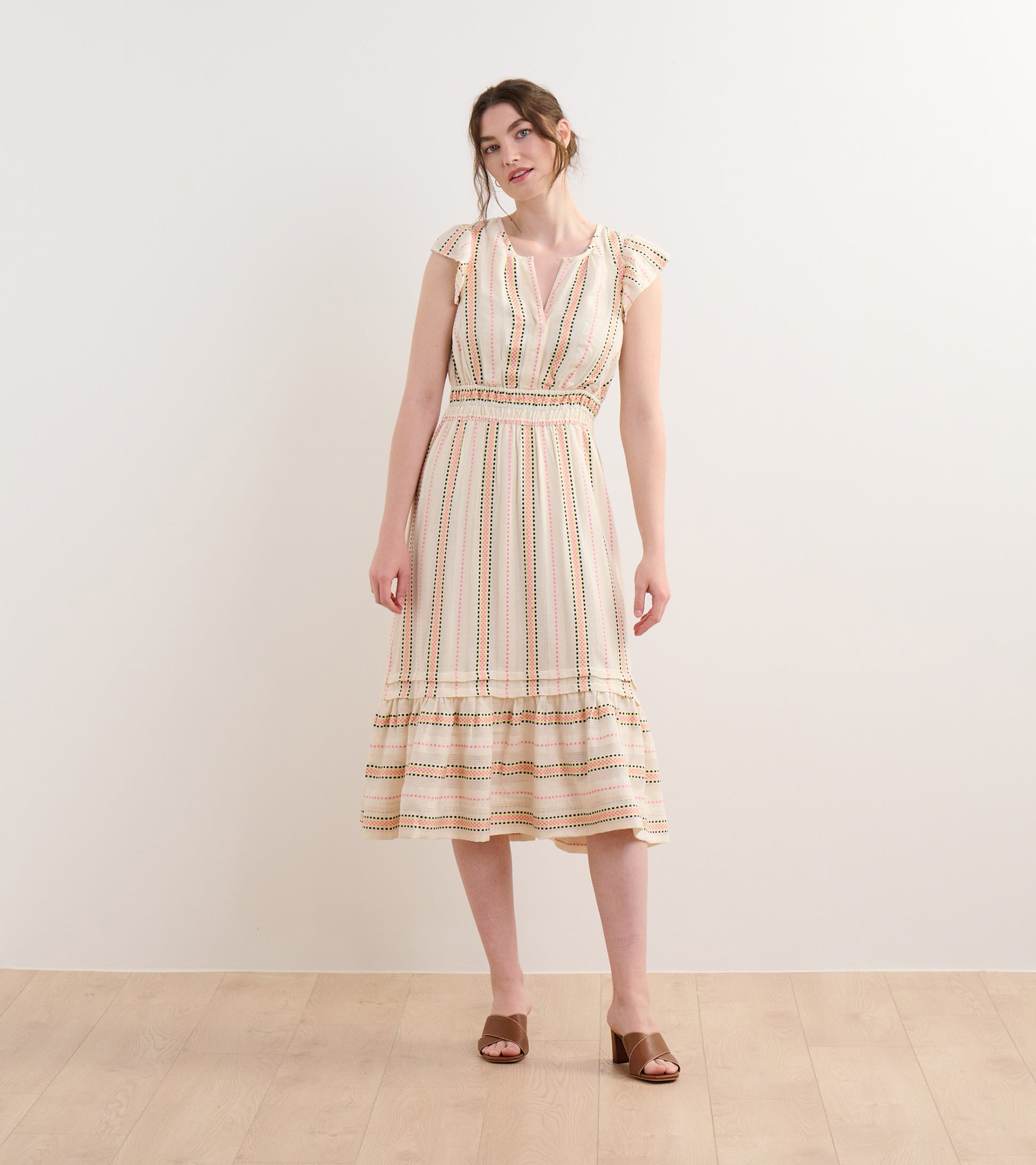 Cream midi dress with multicolor ribbon weave stripes, flutter sleeves, and tiered hem, worn on a model front view