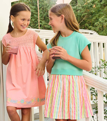 Girl wearing an apricot blush sleeveless dress with crochet bodice and floral embroidery at the hem