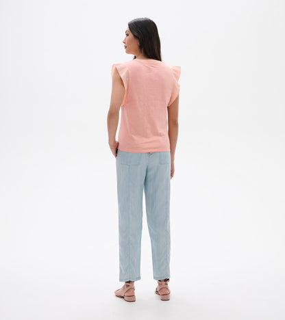 Back view of a sleeveless apricot blush tank top with ruffled shoulders and a crew neck, worn with light blue pants.