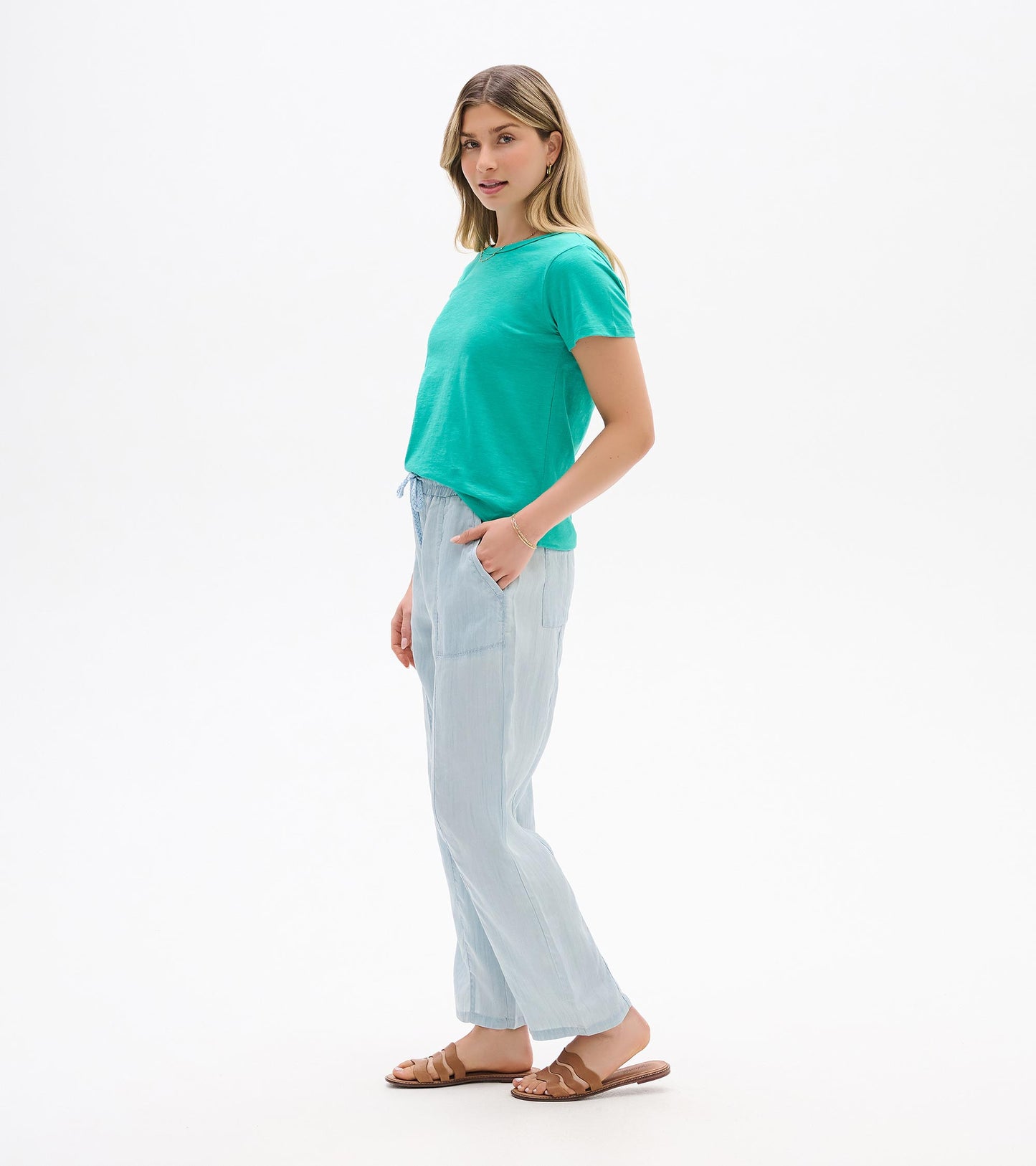 Woman wearing a turquoise short-sleeve crew neck tee with light blue pants, side view