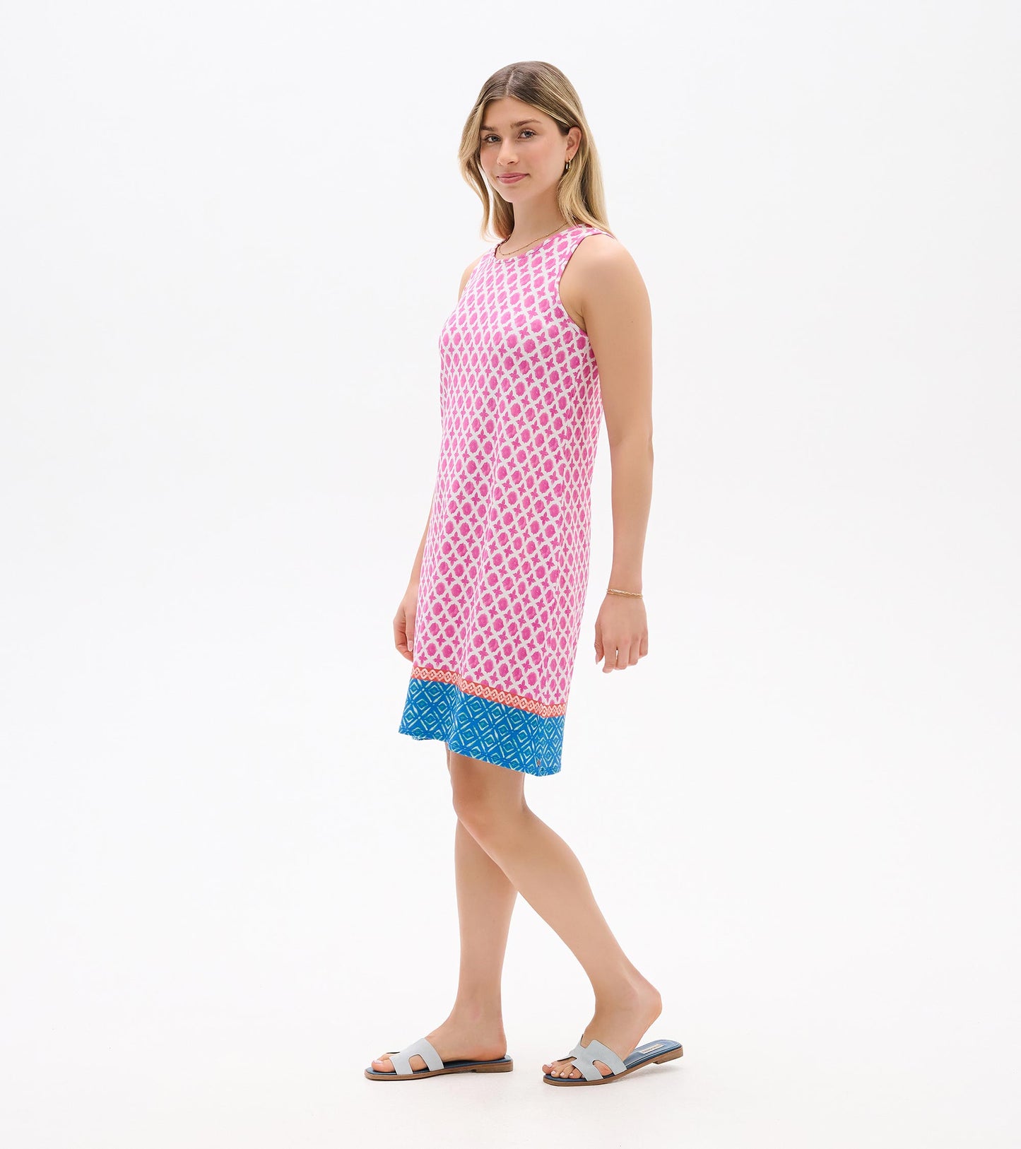 Sleeveless pink patterned shift dress with blue hem, shown on a model in side view