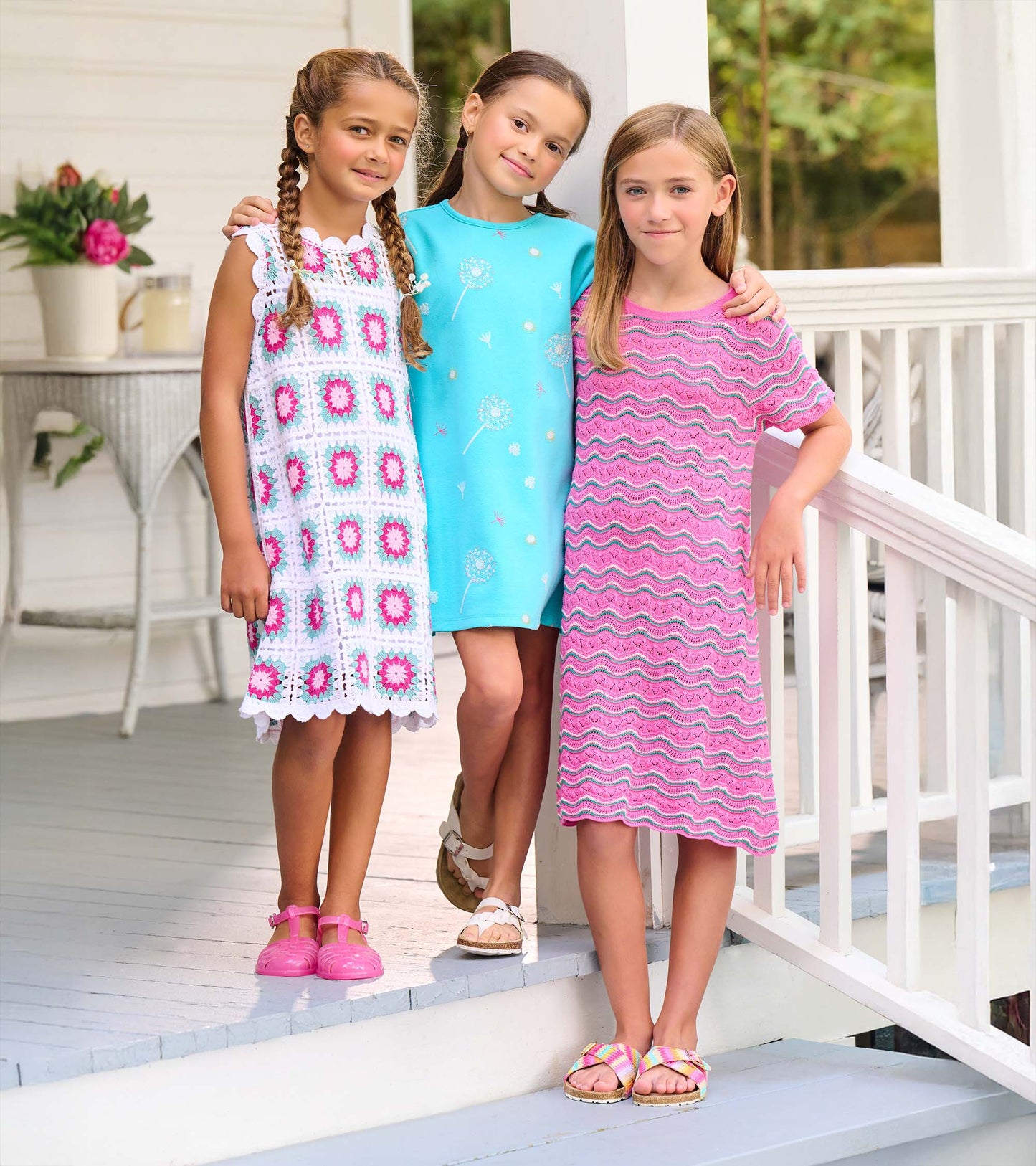 Girls sleeveless crochet dresses in pink, turquoise, and white with floral and wavy patterns, front view on models