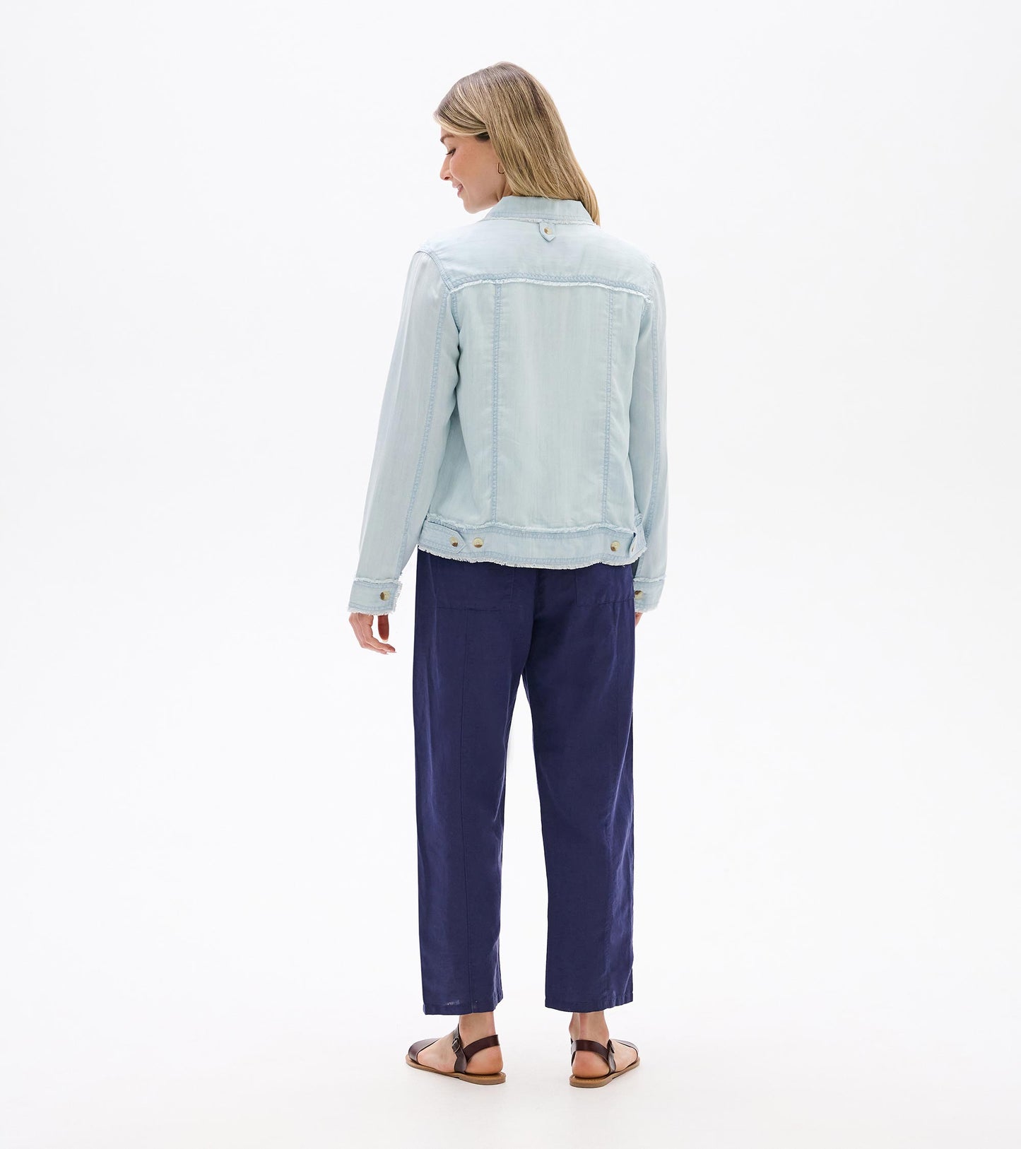 Back view of a light blue denim-style jacket with long sleeves, collar, and button details on a model