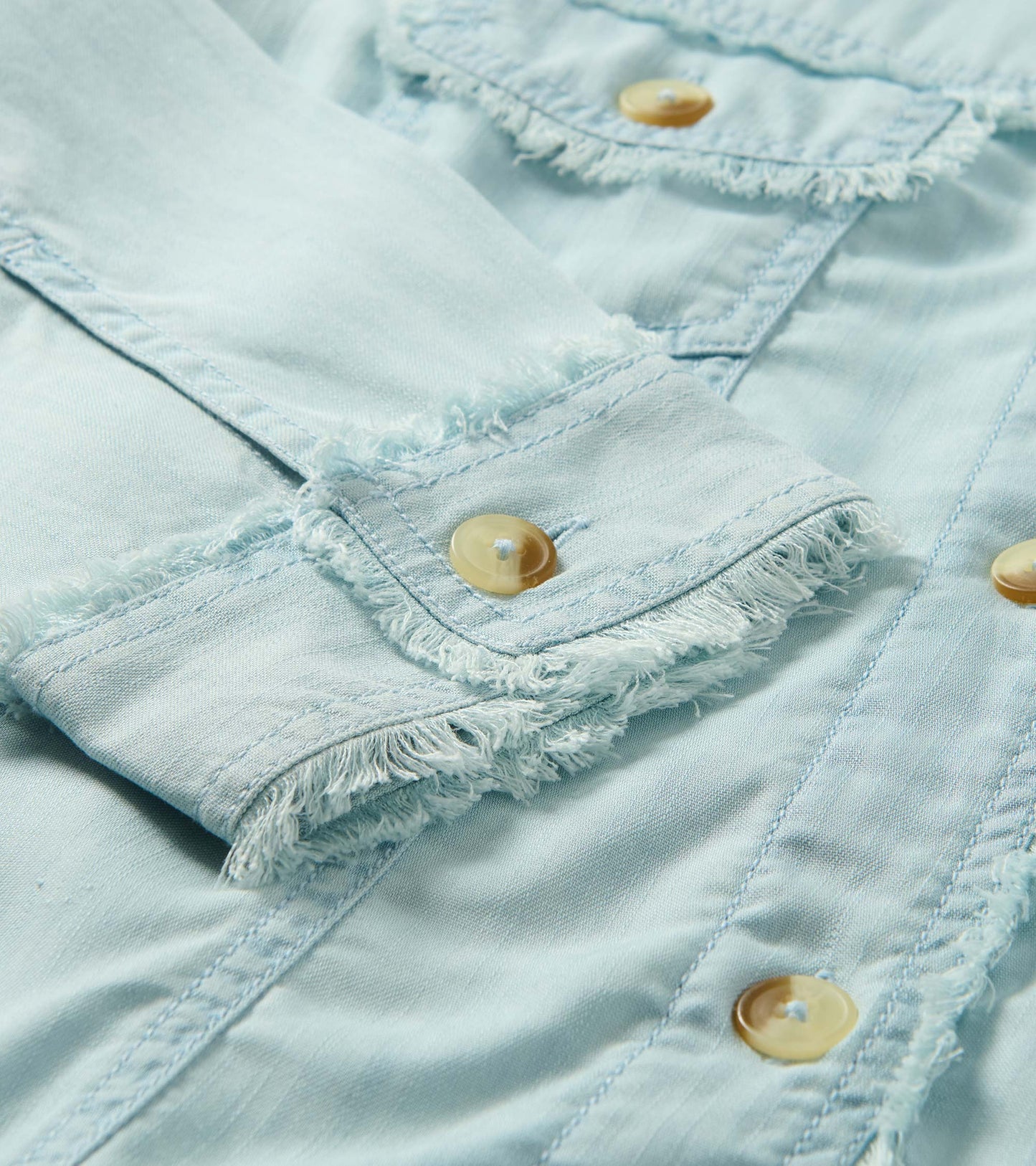 Close-up of a soft blue denim jacket with frayed seams and tan buttons