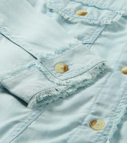 Close-up of a soft blue denim jacket with frayed seams and tan buttons