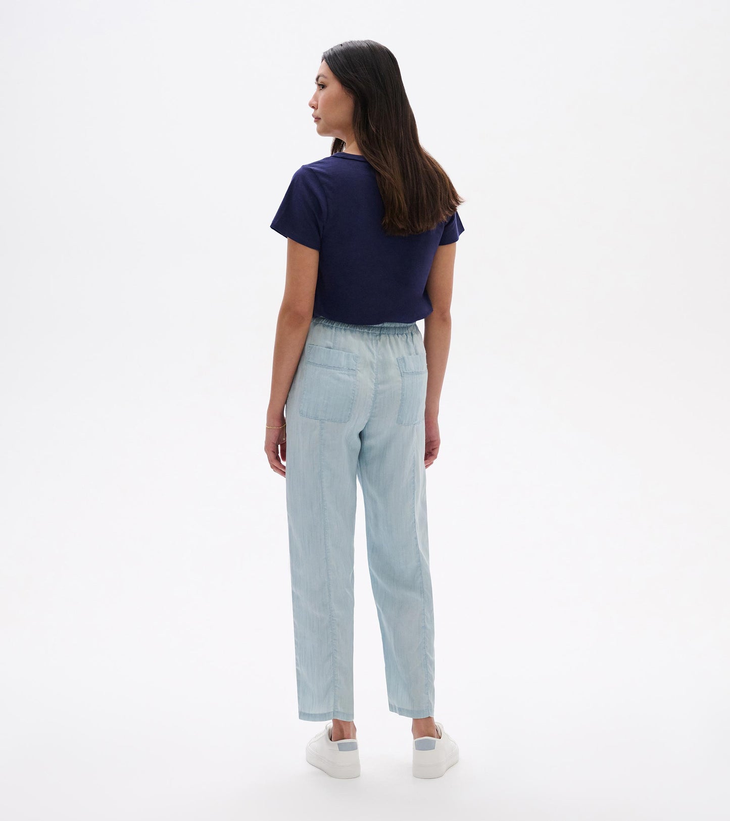Back view of light blue straight-leg pants with elastic waist and patch pockets, worn with white sneakers