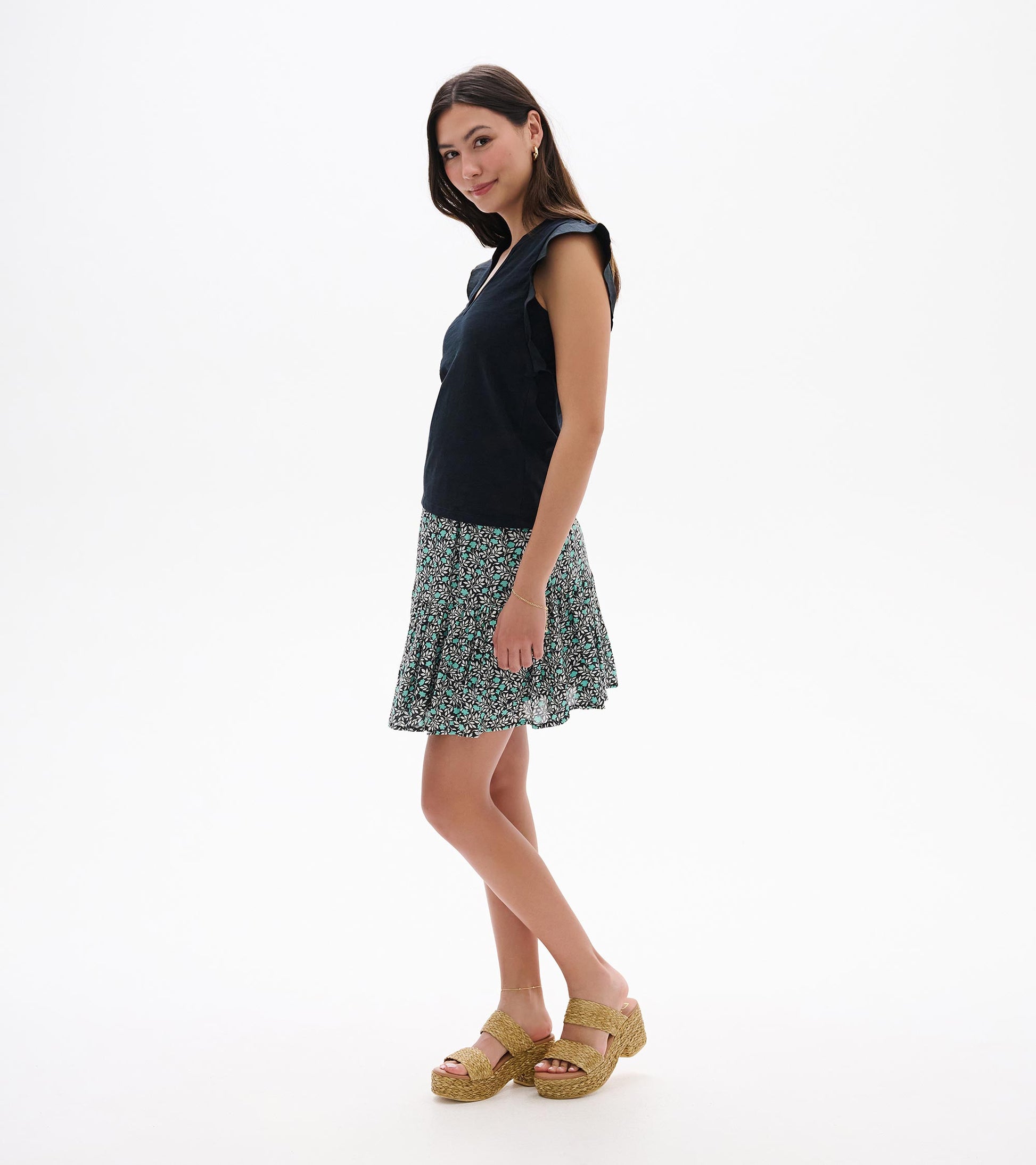 Sleeveless navy tank top with ruffled shoulders, shown with a black, teal, and white floral skirt on a model.
