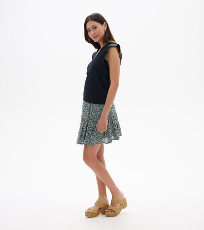 Sleeveless navy tank top with ruffled shoulders, shown with a black, teal, and white floral skirt on a model.