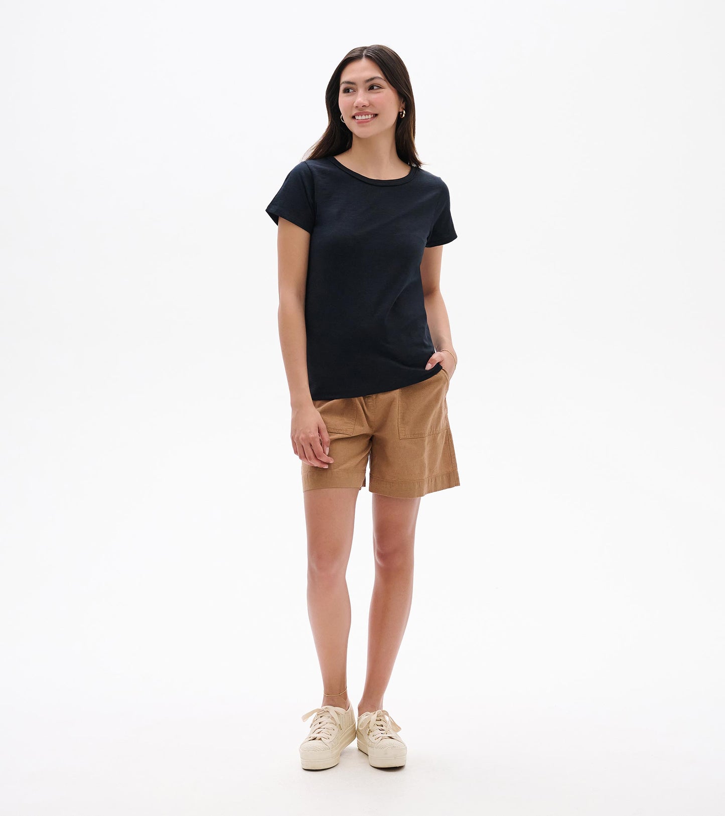 Woman wearing a black crew neck short-sleeve tee, front view, with tan shorts and sneakers.