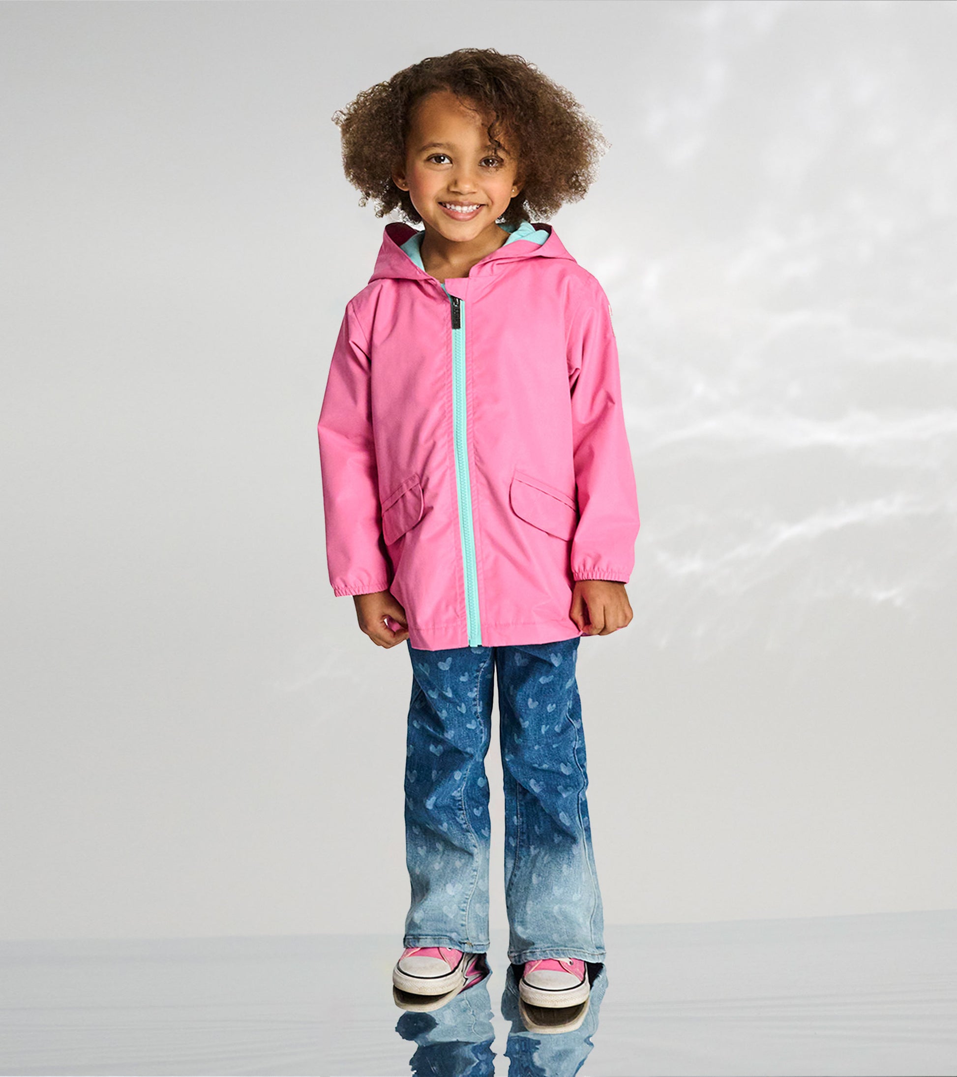 Girl wearing a pink hooded rain jacket with teal zipper and lining, shown front view.