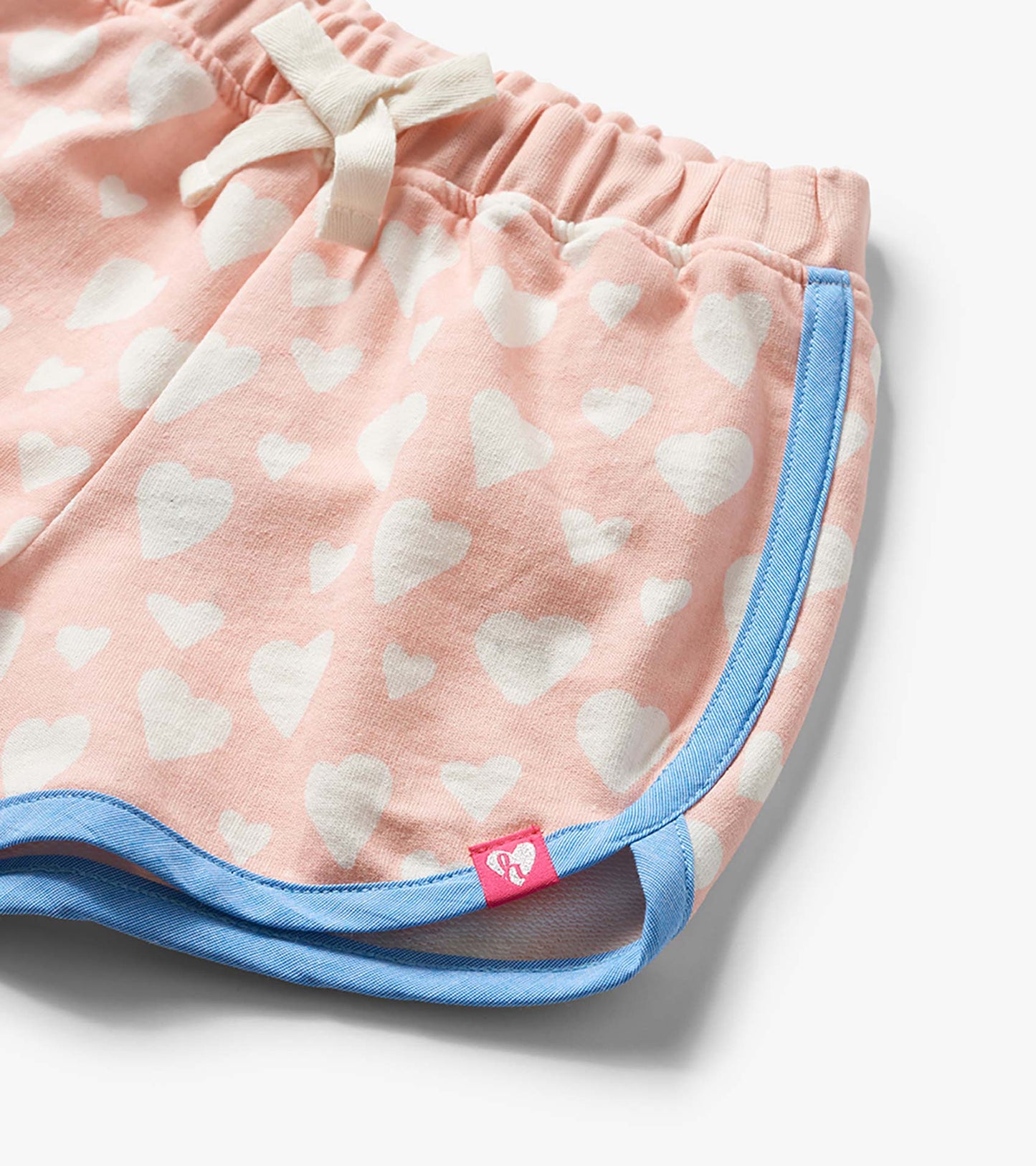 Pink toddler shorts with white heart print, blue trim, and elastic waistband with drawstring