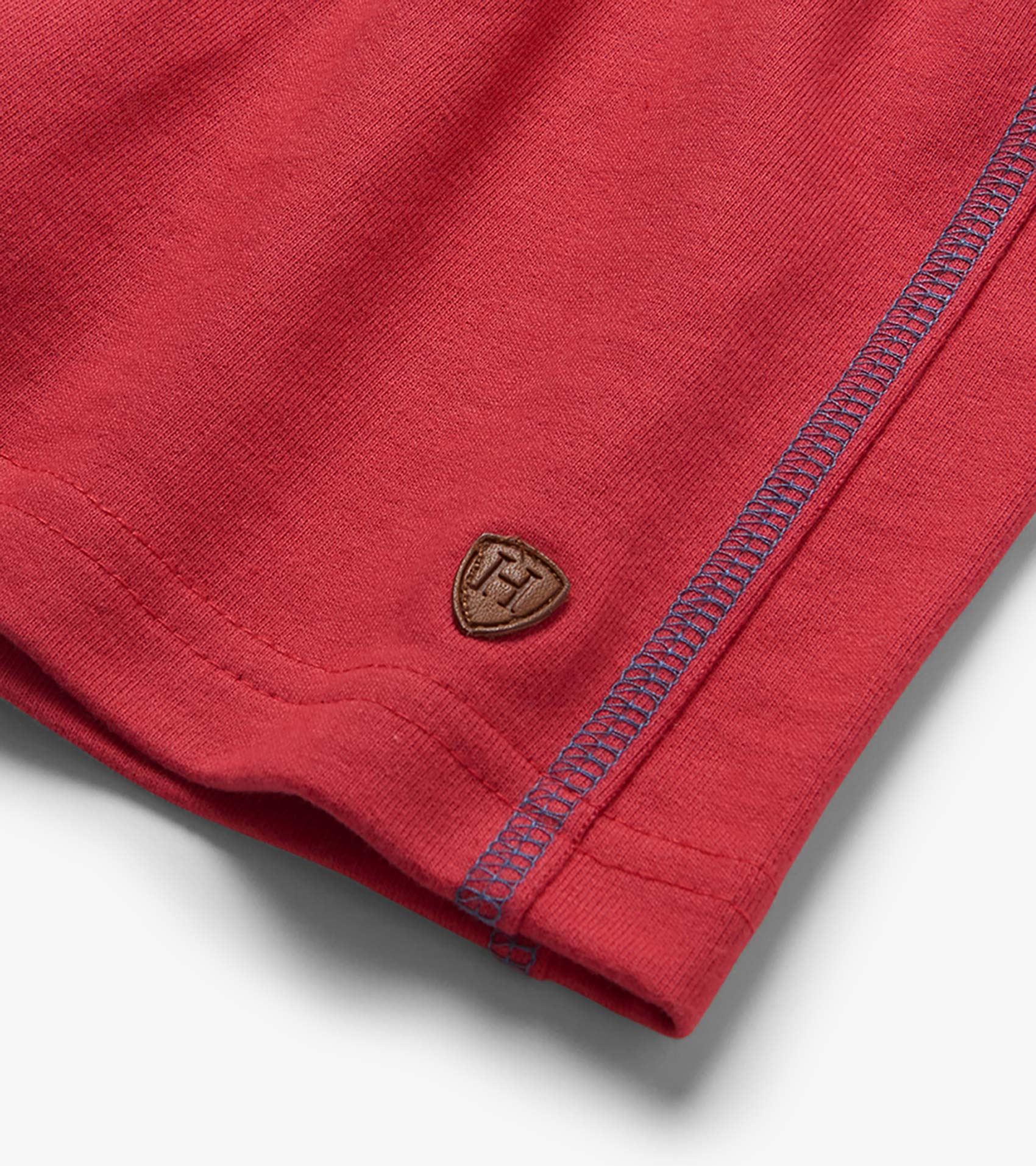 Red French terry shorts with blue contrast stitching and small logo patch at hem