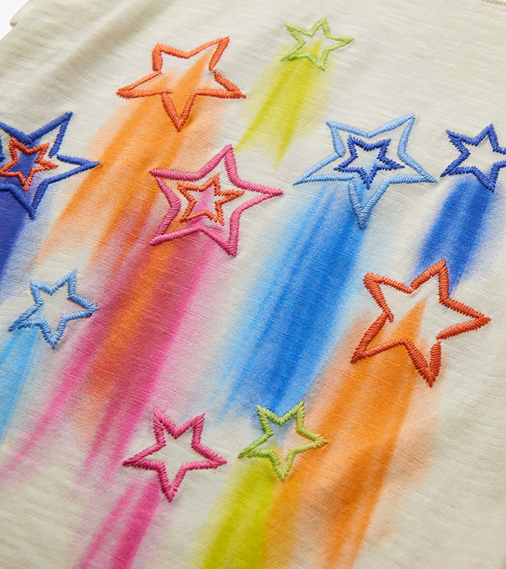 Close-up of cream girls' tee with colorful embroidered falling stars and rainbow streaks