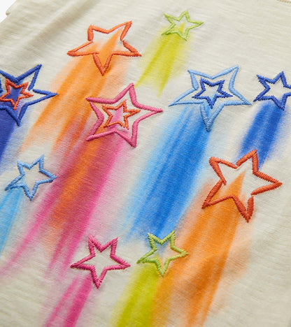 Close-up of cream girls' tee with colorful embroidered falling stars and rainbow streaks