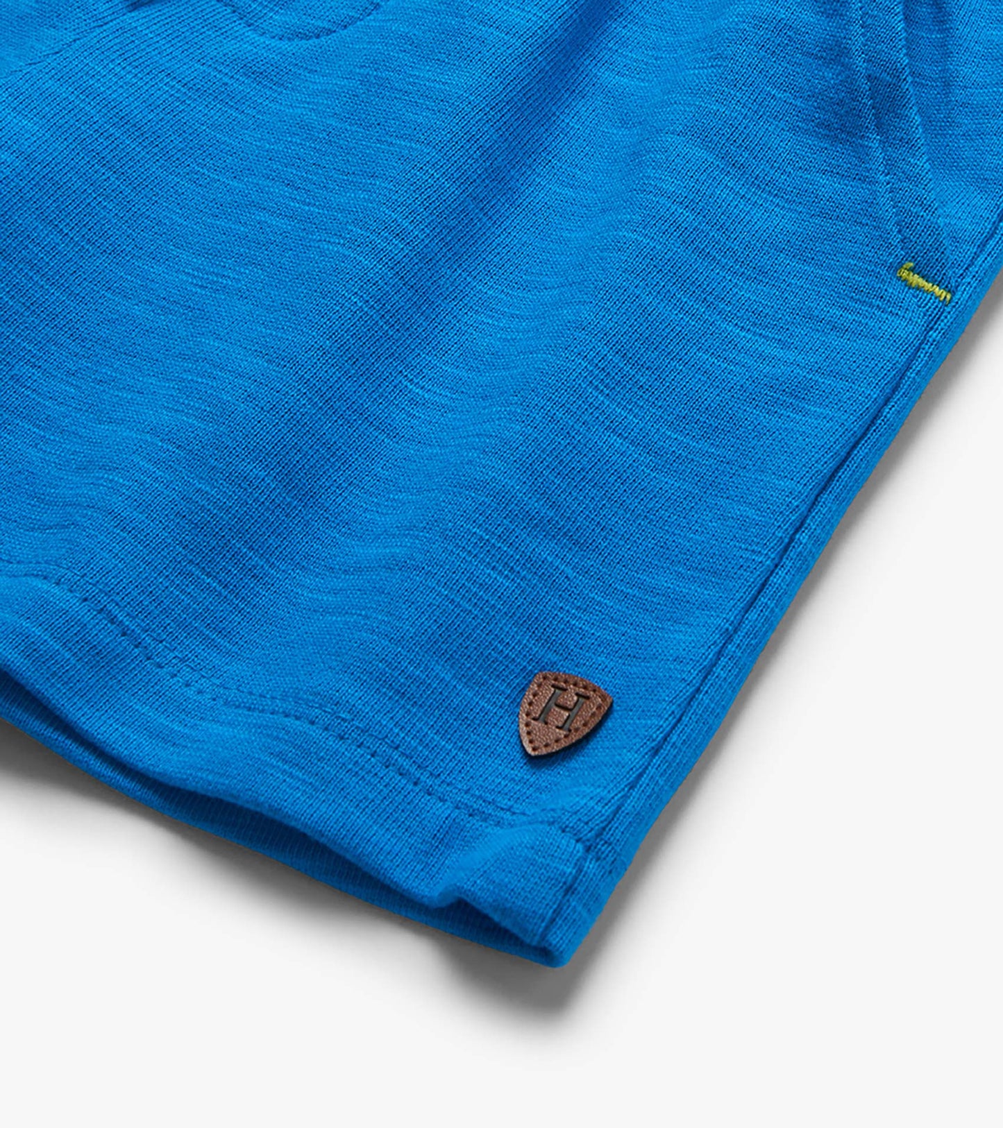Close-up of bright blue knit shorts hem with small brown patch detail and stitched seam, folded view