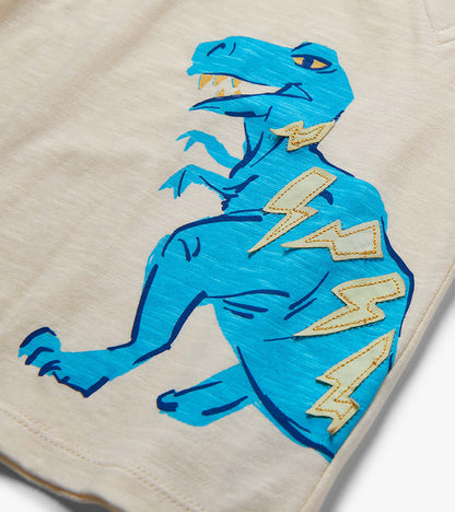 Close-up of beige shorts with a blue dinosaur graphic and lightning bolt patches on the leg.