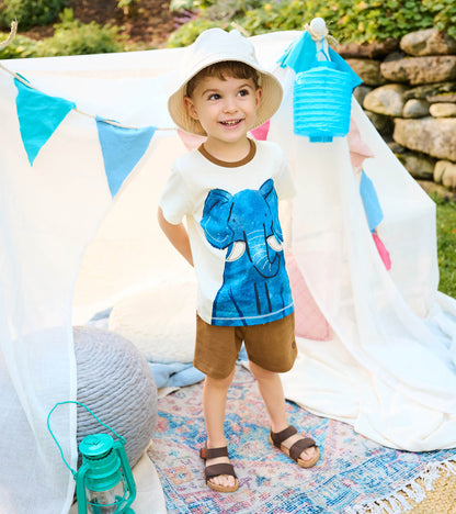 Toddler wearing cream elephant graphic T-shirt and brown shorts set, standing outdoors