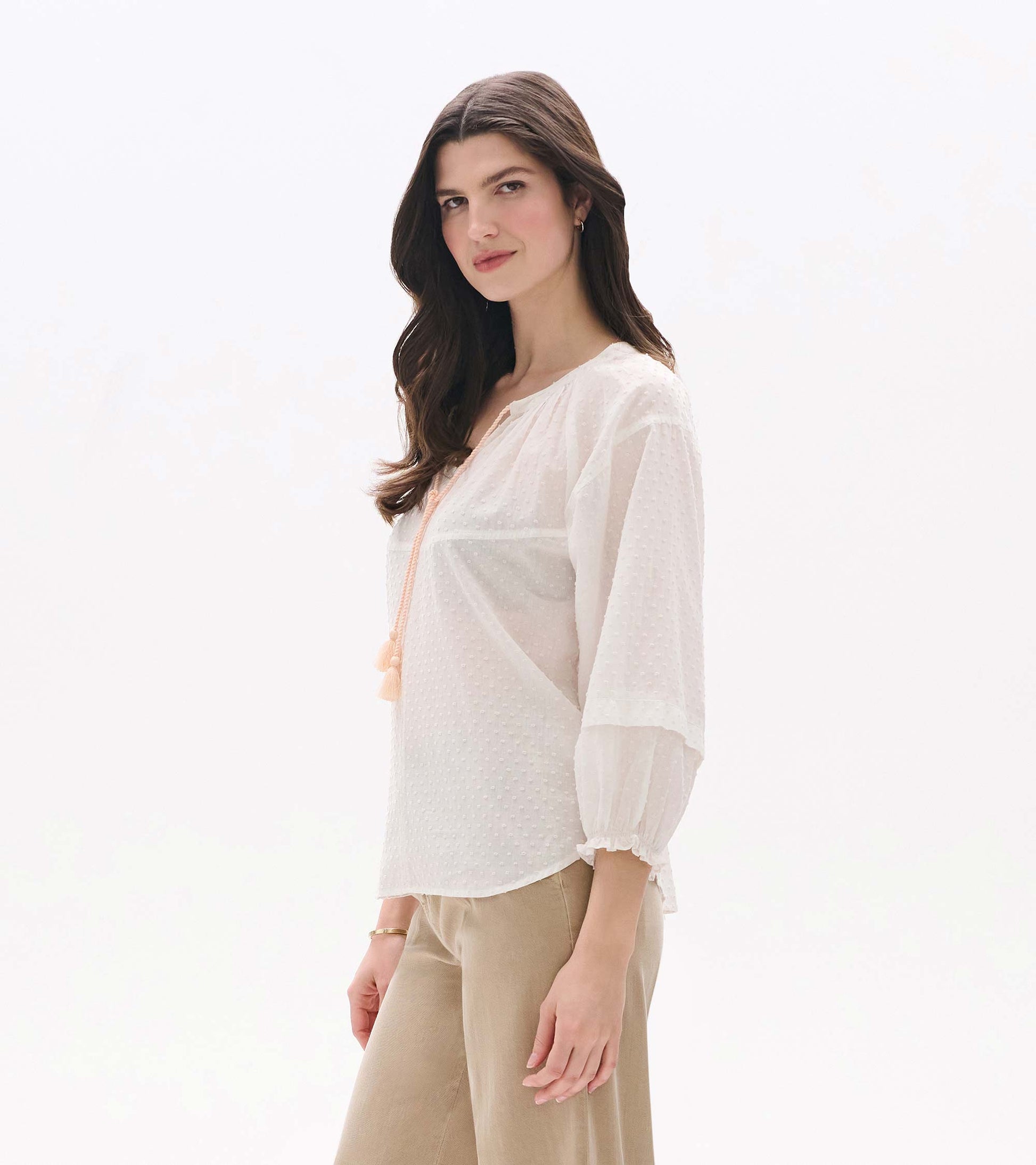 Sheer blush Swiss dot blouse with long puff sleeves and tassel tie neckline, shown on model from the front