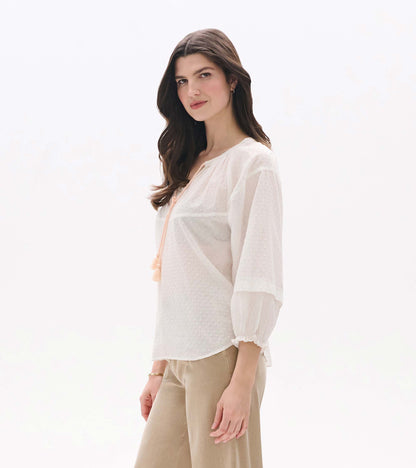 Sheer blush Swiss dot blouse with long puff sleeves and tassel tie neckline, shown on model from the front
